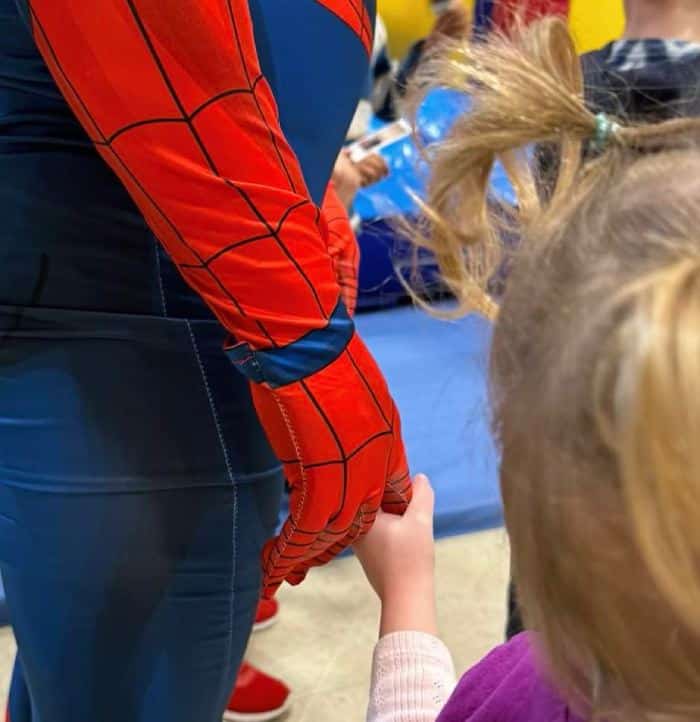 A child lovingly holds the hand of a "superhero" volunteering at Foster Parents Night Out, an Every Child Oregon program that provides respite services for families experiencing foster care.