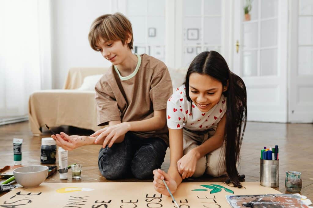 

The power of cultural continuity. Two children sit on the floor, painting a large poster together, in a bright living room.
