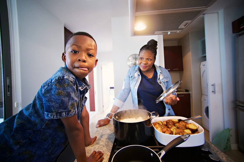 Foster care family cooking together in a modern kitchen, adult and child preparing a meal with potatoes and rice.